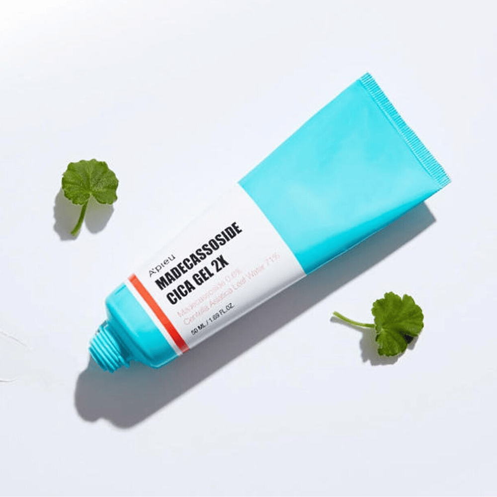 A'pieu Madecassoside Cica Gel 2X en tubo azul con etiqueta blanca, rodeado de tres hojas de centella asiática verde sobre fondo blanco.
