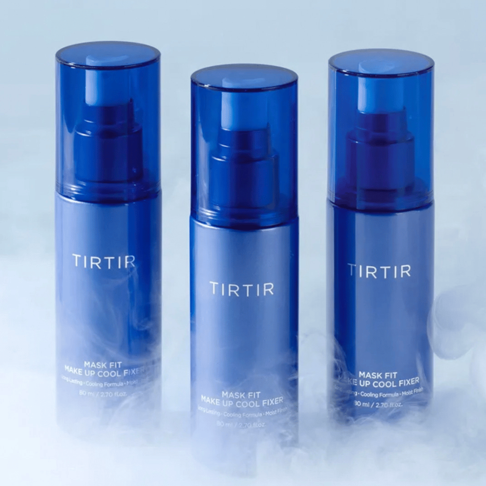 Tres botellas de spray azules con "TIRTIR Mask Fit Make Up Cool Fixer" en la etiqueta. Cada botella contiene 80 ml (2,70 fl. oz.) y está diseñada para proporcionar una sensación refrescante y un maquillaje duradero. Las botellas están colocadas sobre un fondo claro con niebla para crear una atmósfera de frescura.