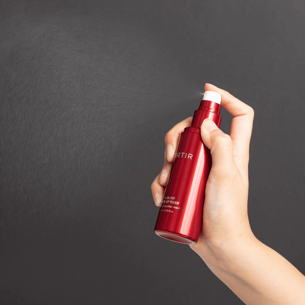 Una mano sosteniendo una botella roja de la marca tirtir Mask Fit Make Up Fixer y rociando una fina niebla, ideal para fijar el maquillaje.