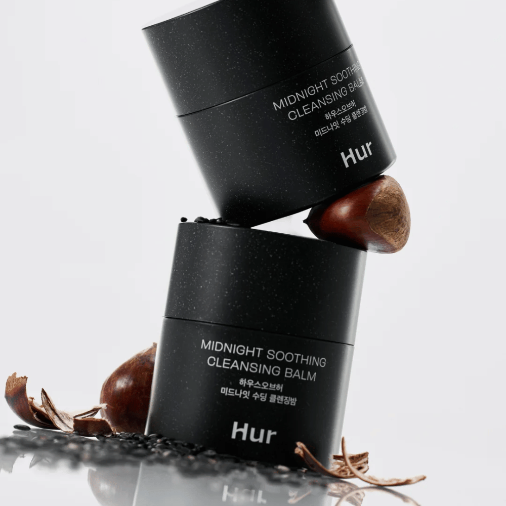 Dos frascos de Cómo Midnight Soothing Cleansing Balm apilados con ingredientes naturales. Bálsamo limpiador nutritivo para la limpieza diaria de pieles sensibles.
