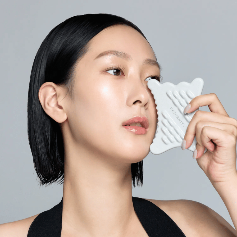Primer plano de una modelo usando RETURNITY Mini Guasha alrededor de la zona de los ojos y las mejillas para masaje y cuidado relajante de la piel.