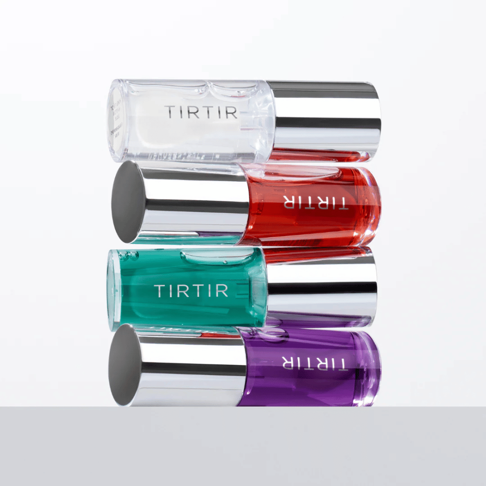 Cuatro TIRTIR My Glow Lip Oil en diferentes colores: transparente, rojo, verde y lila, apilados uno sobre otro con tapas plateadas sobre fondo blanco.