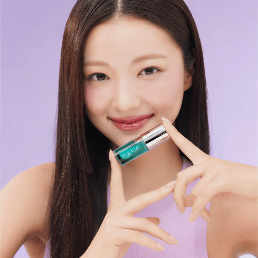 Mujer con cabello largo y lacio sosteniendo TIRTIR My Glow Lip Oil y mostrando sus labios brillantes y rosados sobre un fondo lila.