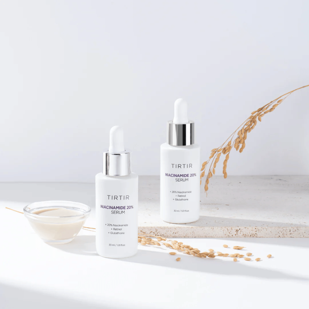 Dos botellas de Tirtirs "Niacinamide 20% Serum" se muestran sobre una superficie clara junto con un pequeño cuenco con una sustancia cremosa y algunas hebras de plantas secas. El suero contiene 20 % de niacinamida, retinol y glutatión, lo que ayuda a mejorar el aspecto y la textura de la piel.