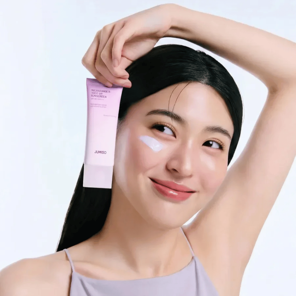 La modelo sostiene JUMISO Niacinamide 3+ Tone-Up Sunscreen SPF50+ PA++++ – crema solar con niacinamida que unifica el tono de la piel y protege la piel.