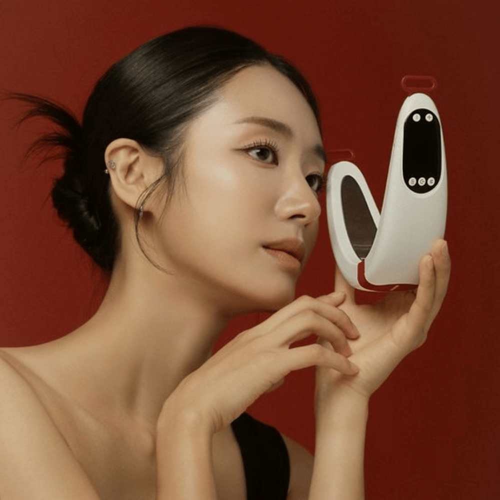 Una modelo sostiene Beaund Nmode Pro frente al rostro sobre un fondo rojo. La imagen destaca el diseño elegante del dispositivo, la pantalla digital y el formato compacto.