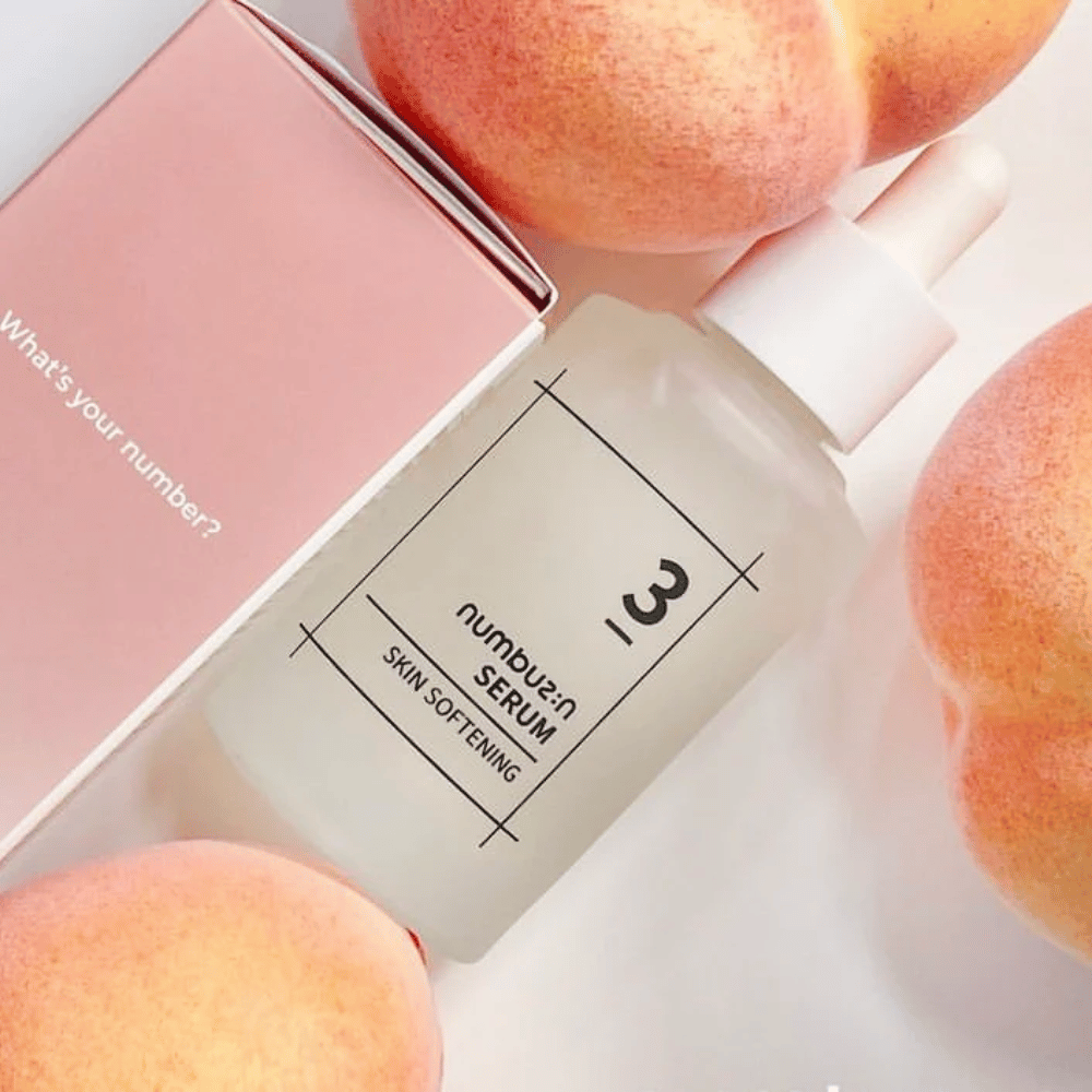 Botella con numbus:in No.3 Skin Softening Serum rodeada de duraznos y una caja rosa con el texto "¿Cuál es tu número?".