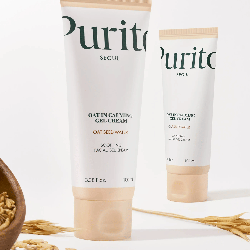 Purito Oat-In Calming Gel Cream en tubo beige, colocado con granos de avena. Calma la piel sensible con agua de avena y textura de gel ligera.