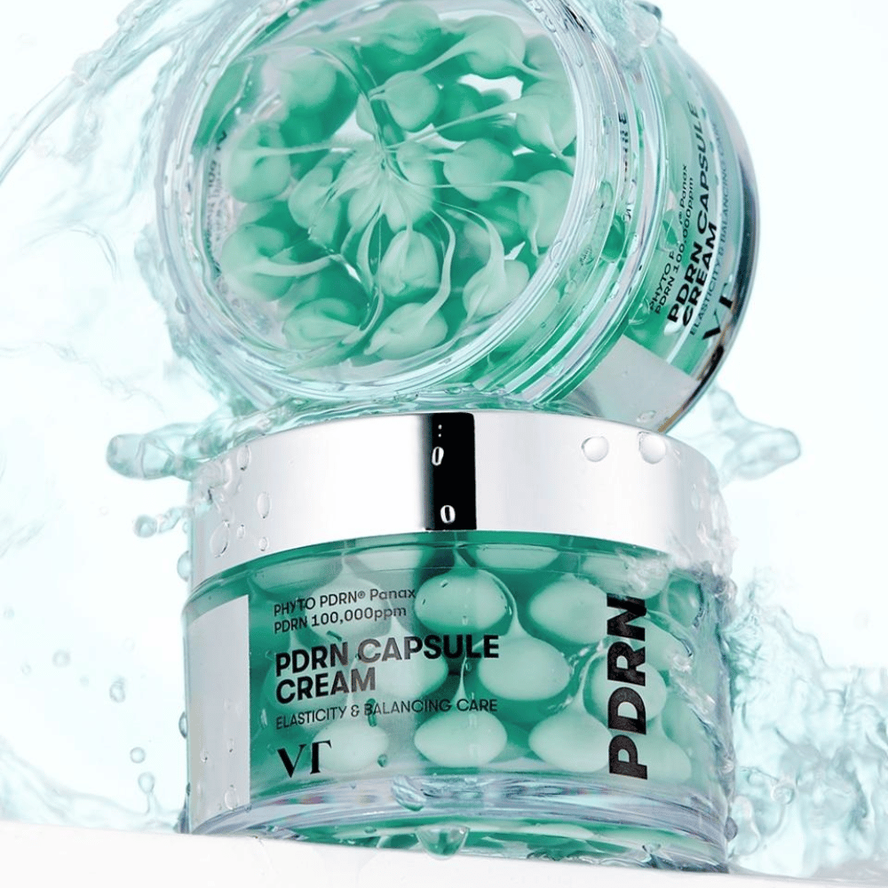 Dos frascos de VT PDRN Capsule Cream apilados con salpicaduras de agua alrededor. Los frascos transparentes muestran cápsulas verdes en el interior, con el texto "Elasticity & Balancing Care" visible en la etiqueta.
