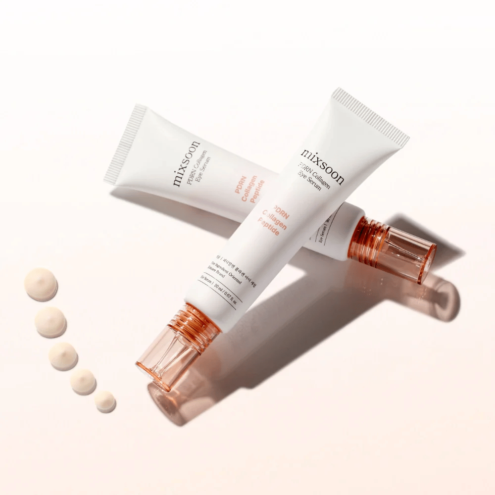 Dos tubos de Mixsoon PDRN Collagen Eye Serum están cruzados con pequeñas gotas del suero. Un tratamiento ligero para los ojos que hidrata y suaviza las líneas.