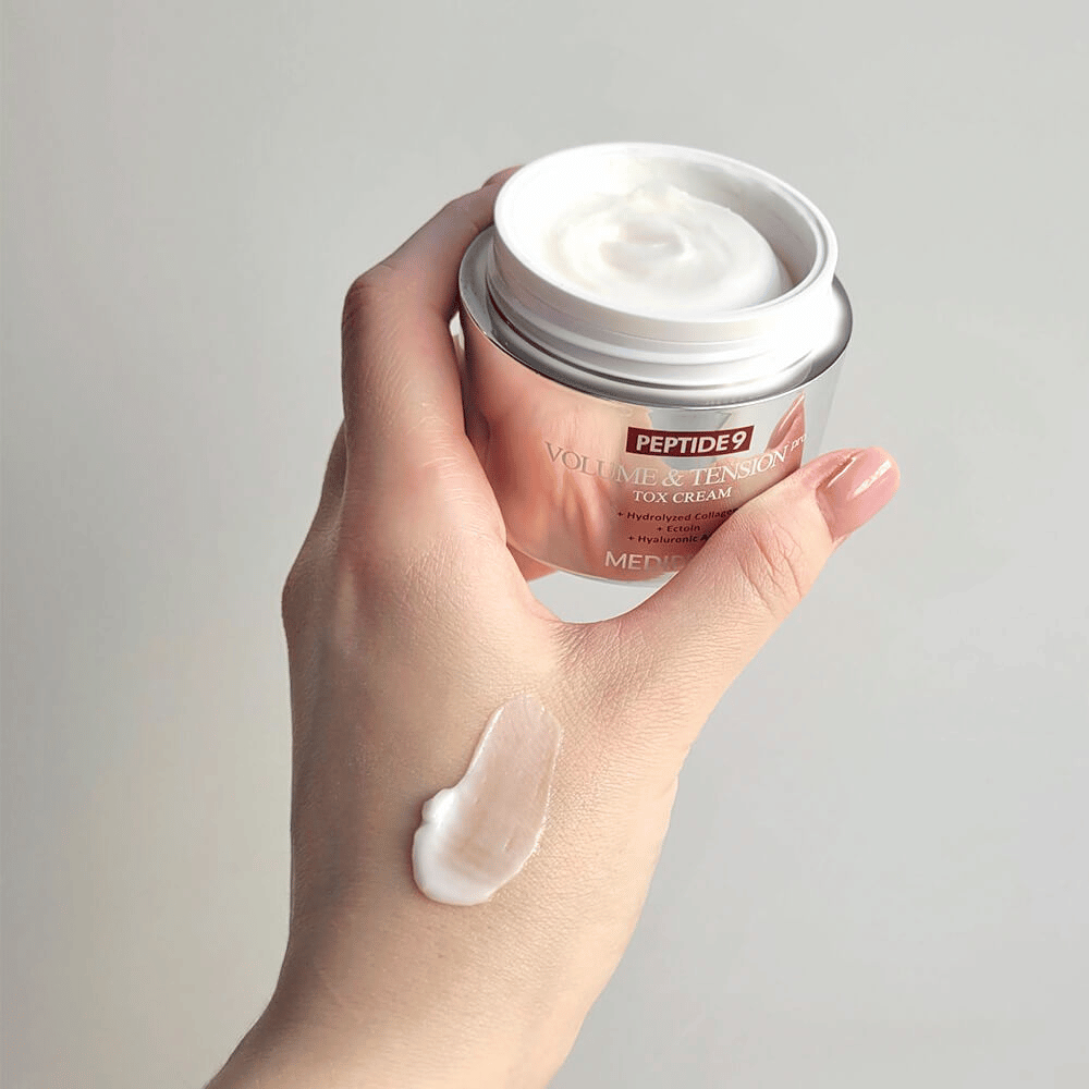 Mano sosteniendo MEDI-PEEL Peptide 9 Volume & Tension Tox Cream con un poco de crema en el dorso de la mano. La fórmula sedosa hidrata y proporciona firmeza y elasticidad a la piel.