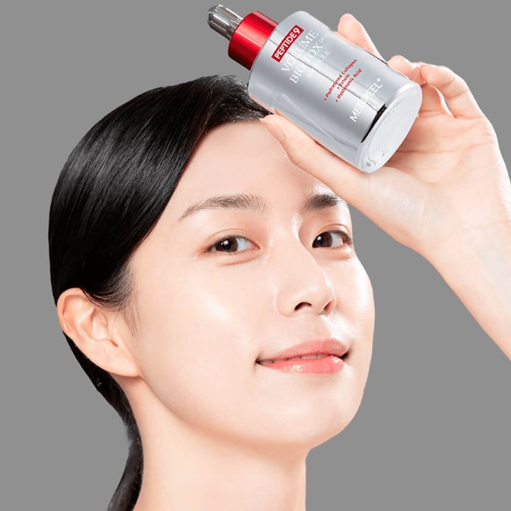 Persona sosteniendo MEDI-PEEL Peptide 9 Volume Bio Tox Pro Ampoule contra la frente. La piel se ve hidratada y radiante: el suero fortalece la elasticidad y firmeza.
