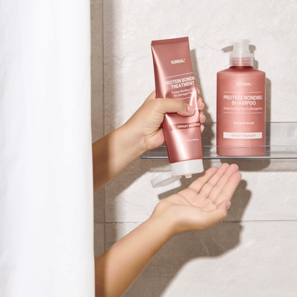 KUNDAL Protein Bonding Treatment Violet Muguet se utiliza en la ducha, con Protein Bonding Shampoo colocado en la estantería al lado.