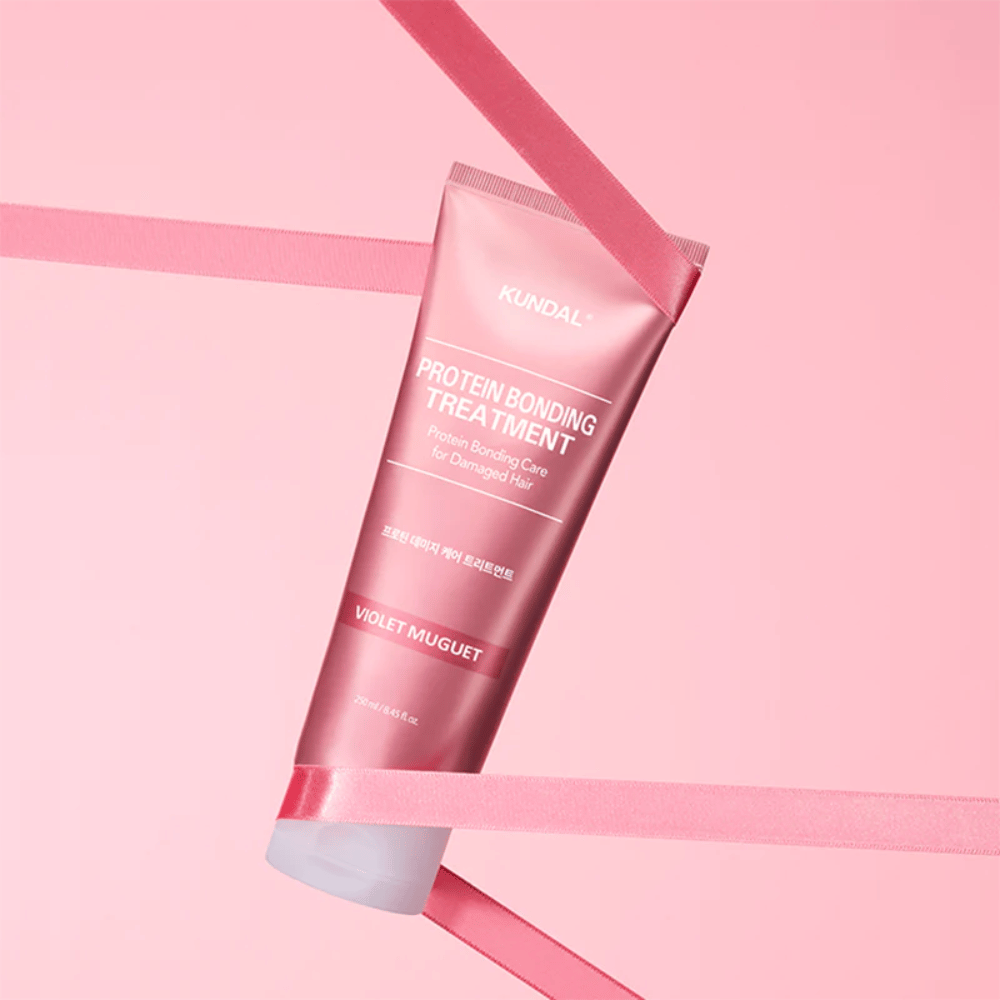 KUNDAL Protein Bonding Treatment Violet Muguet en tubo rosa 250 ml contra un fondo rosa con cintas decorativas.