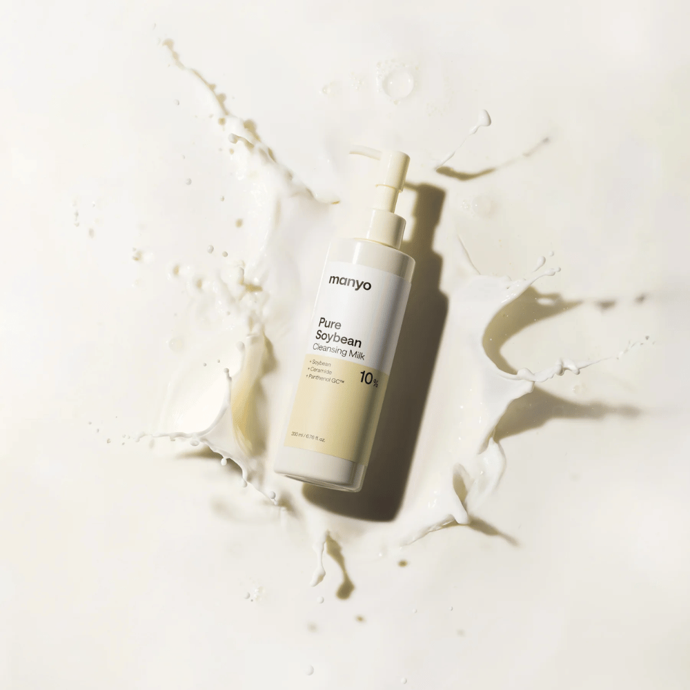 1. Ma:nyo Pure Soybean Cleansing Milk – leche limpiadora suave con soja en botella con dosificador rodeada de salpicaduras de leche sobre fondo claro