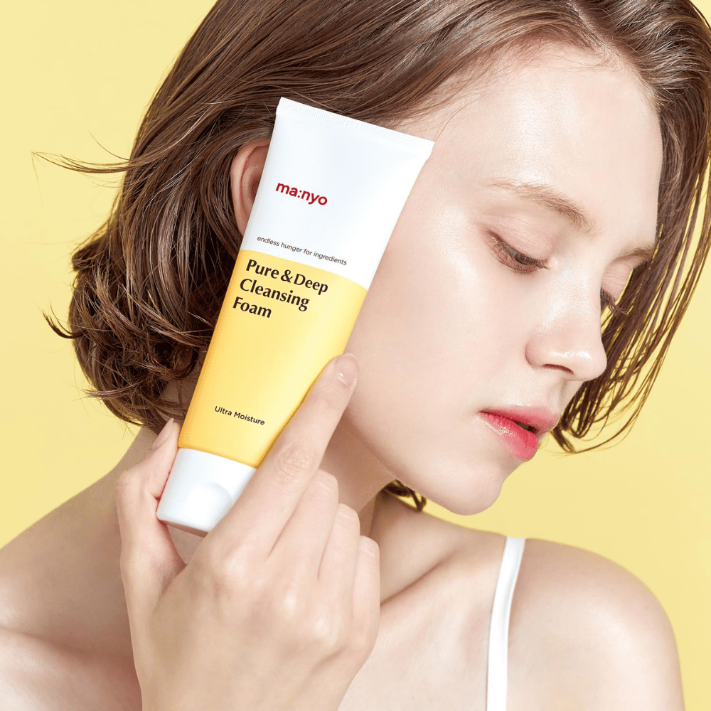 Mujer con piel saludable e hidratada sostiene Ma:nyo Pure & Deep Cleansing Foam - limpiador facial suave que aporta brillo y equilibrio con ingredientes naturales.