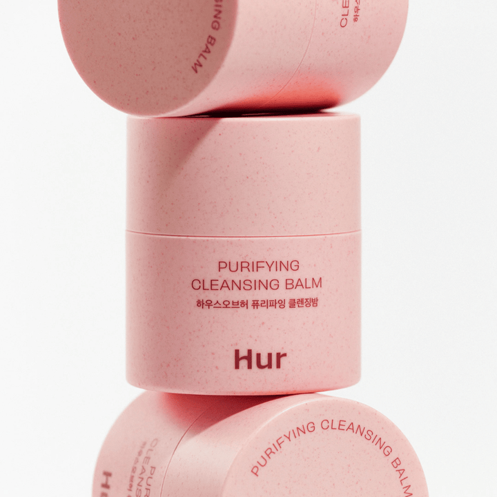 Cómo Purifying Cleansing Balm en envase rosa apilado en estudio. Bálsamo limpiador que disuelve eficazmente el maquillaje, el sebo y las impurezas sin resecar la piel.