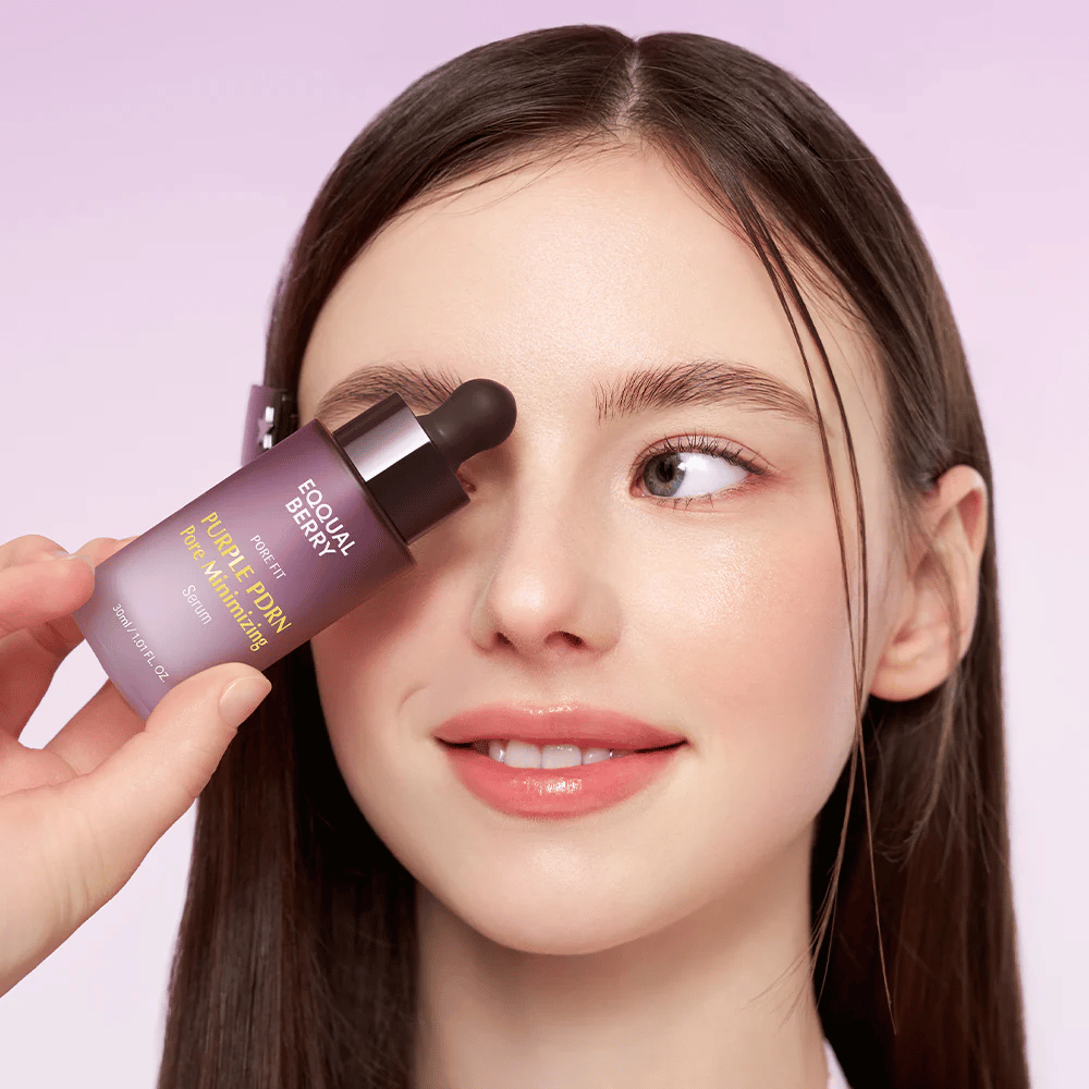 Mujer joven con piel lisa sostiene una botella de Equal Berry Purple PDRN Pore Minimizing Serum contra la frente, sobre un fondo lila claro.