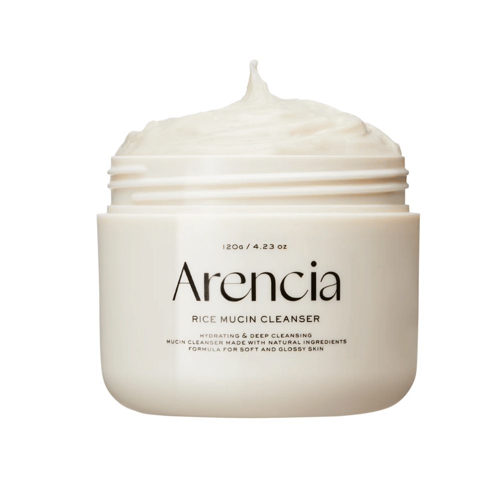Imagen del producto de Arencia Rice Mucin Cleanser en un tarro blanco con textura cremosa y batida que sobresale de la abertura. El texto en el empaque enfatiza la hidratación y la limpieza profunda.