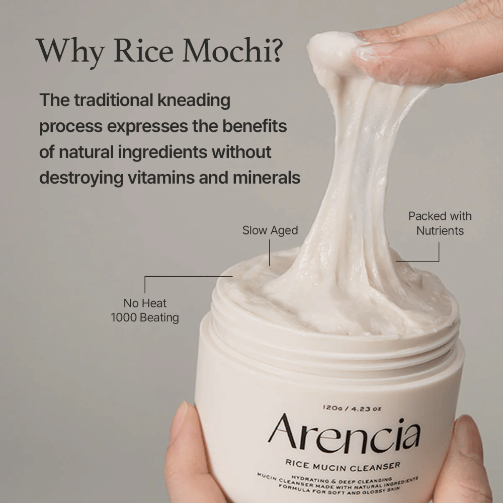 Mano levantando una crema limpiadora blanca y elástica de un tarro marcado "Arencia Rice Mucin Cleanser". El texto describe el amasado tradicional que conserva los nutrientes sin destruir las vitaminas y minerales.