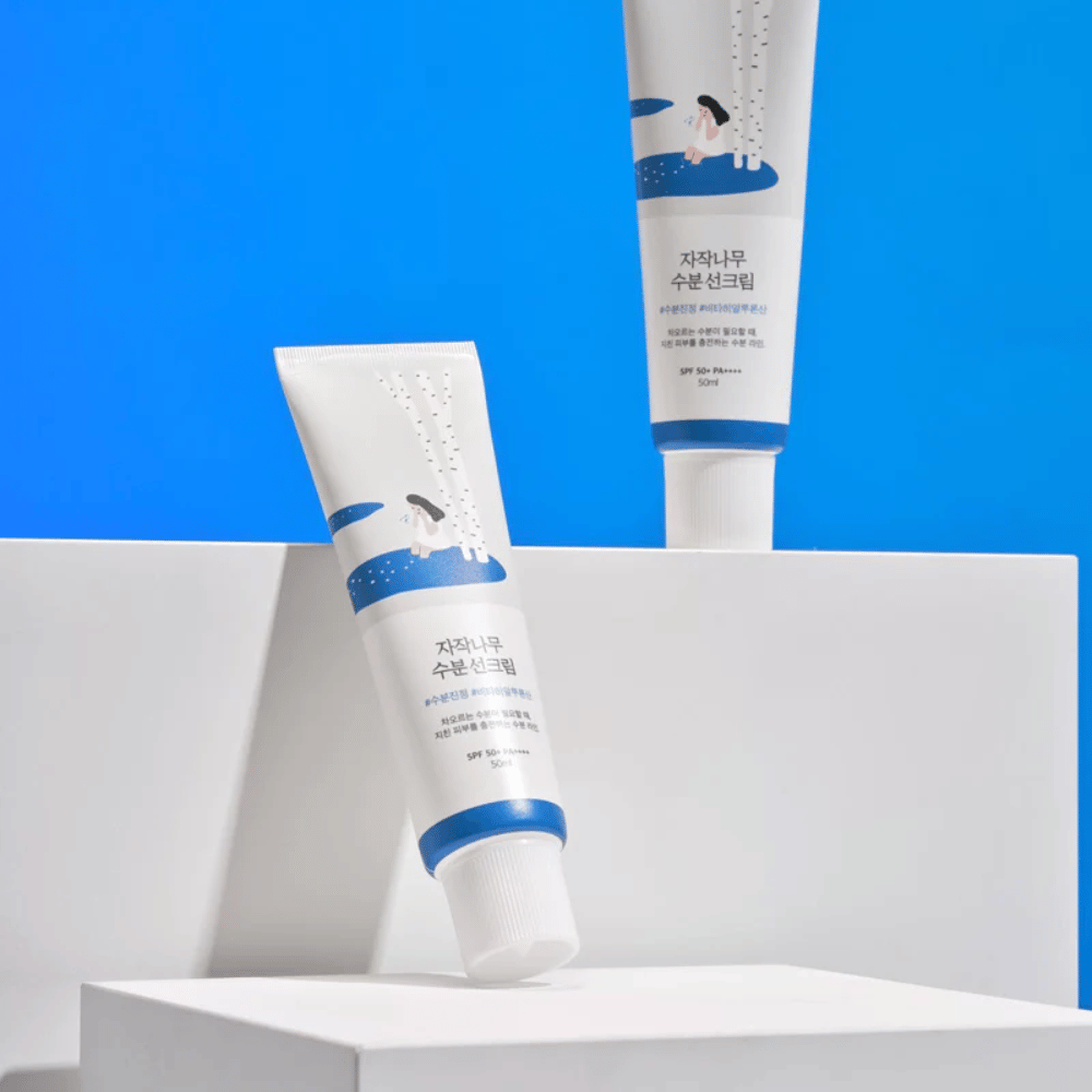 Dos tubos con Round Lab Birch Juice Moisturizing Sunscreen SPF50+ PA++++ 50ml que están sobre un fondo azul.