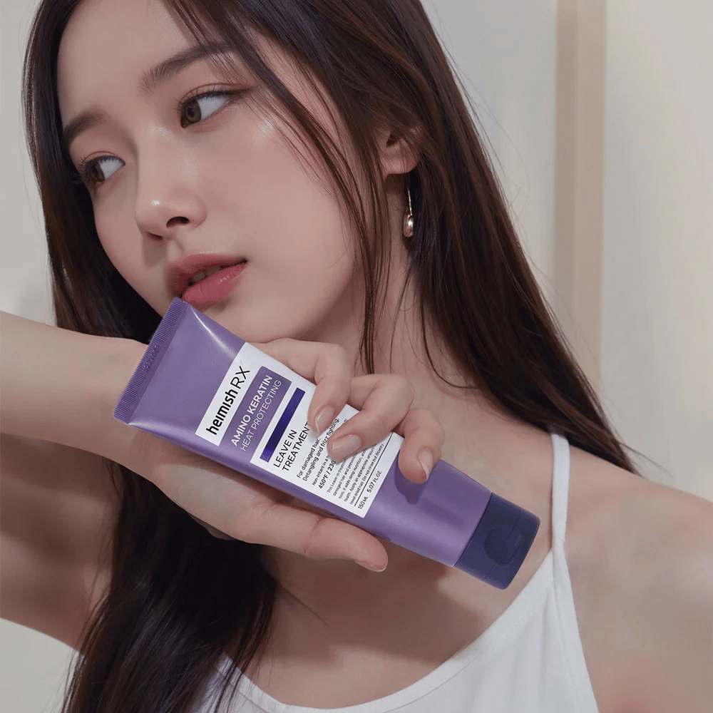 Mujer con cabello largo y brillante sosteniendo Heimish RX Amino Keratin Leave-In Treatment – muestra el producto como un paso de cuidado y protección térmica en la rutina de cuidado capilar.