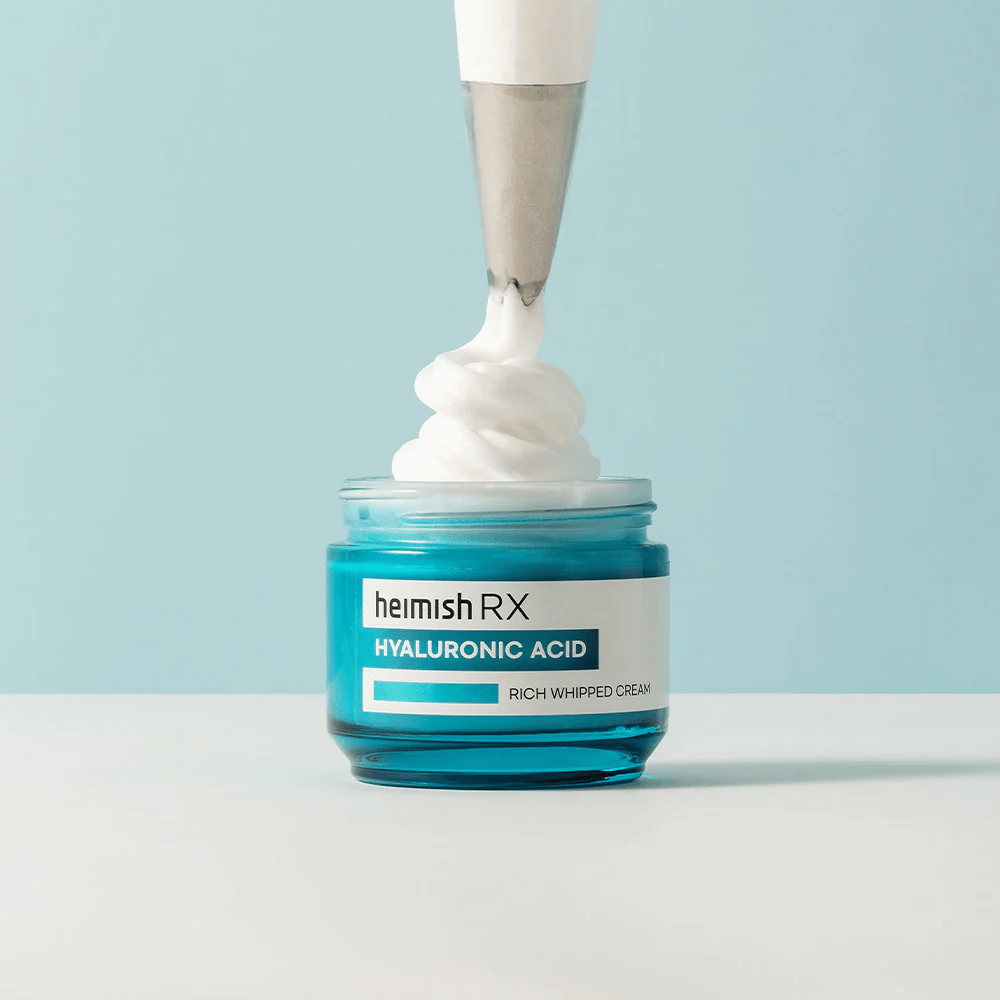 Heimish RX Hyaluronic Acid Rich Whipped Cream en un tarro de vidrio azul, donde una manga pastelera aplica la crema esponjosa. Una crema facial hidratante con ácido hialurónico para una hidratación intensa y una piel suave y rellena.