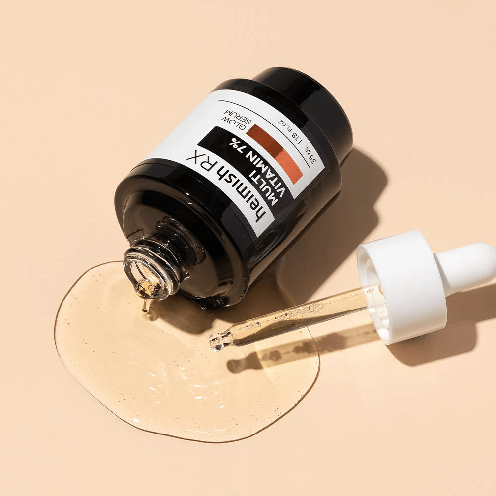 Heimish RX Multi Vitamina 7% Glow Serum sobre un fondo beige con suero esparcido alrededor de la botella y una pipeta llena de producto, destacando su fórmula rica en nutrientes.