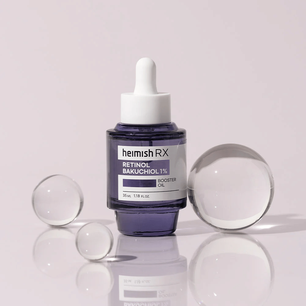 Heimish RX Retinol Bakuchiol Booster Oil 1% en una elegante botella de vidrio morado con pipeta. El aceite está colocado sobre una superficie reflectante con bolas de vidrio alrededor, lo que proporciona una sensación lujosa y moderna.