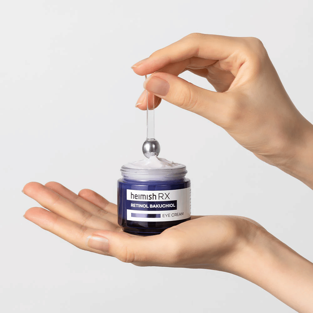 Heimish RX Retinol Bakuchiol Eye Cream en un elegante frasco azul, levantado con un aplicador de metal. Una crema para ojos con retinol y bakuchiol para reducir las líneas finas y proporcionar una piel más firme.