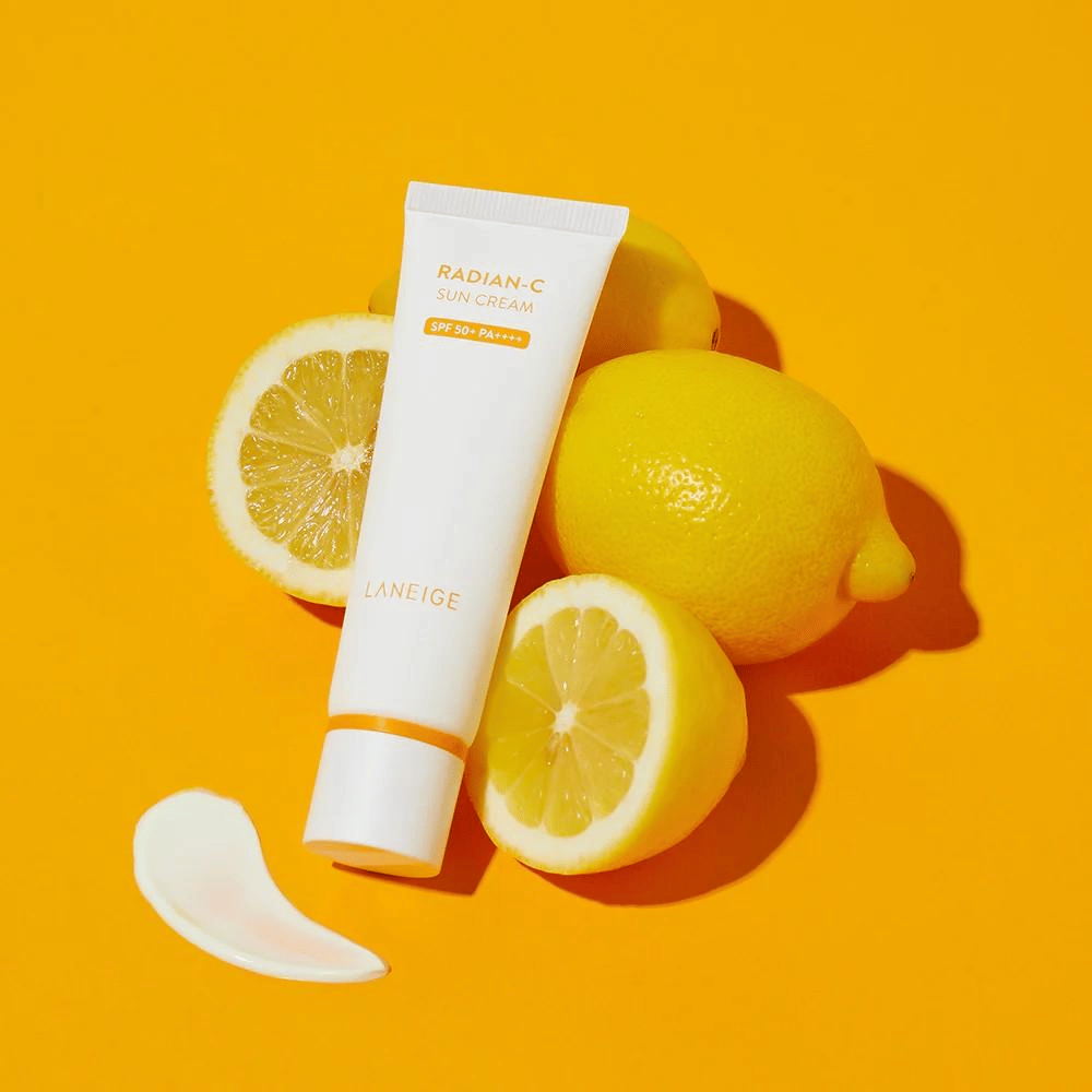 LANEIGE Radian-C Sun Cream SPF 50+ PA++++ con limones y un toque de crema solar sobre un fondo amarillo vibrante.