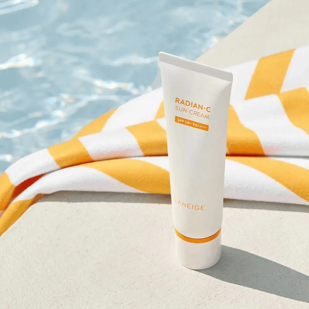 LANEIGE Radian-C Sun Cream está al borde de una piscina con una toalla a rayas amarillas y blancas en el fondo.
