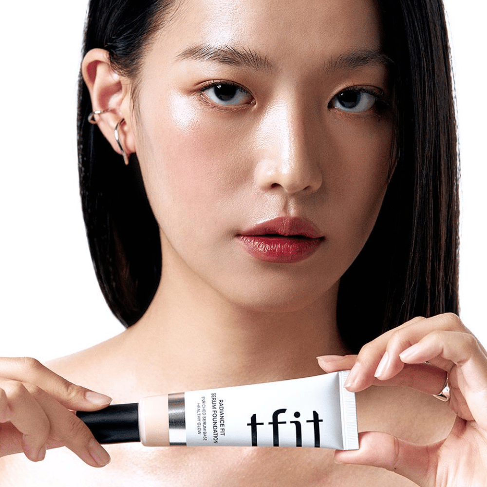 Modelo con piel brillante y lisa sostiene en TFIT Radiance Fit Serum Foundation, lo que resalta el acabado natural y el brillo del producto.