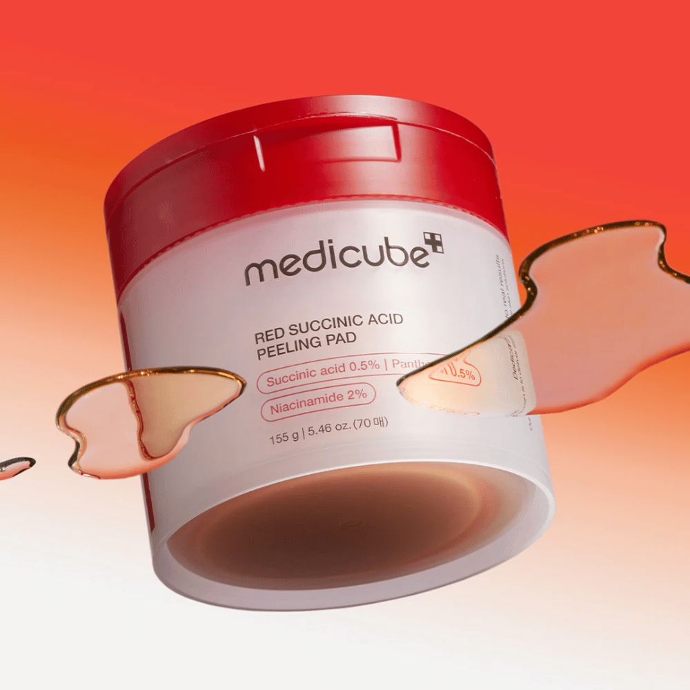 Medicube Red Succinic Acid Peeling Pad en un frasco blanco y rojo, colocado contra un fondo degradado en rojo y naranja. El producto contiene ácido succínico y niacinamida para exfoliación y mejora de la piel. Se observa una textura líquida alrededor del frasco.
