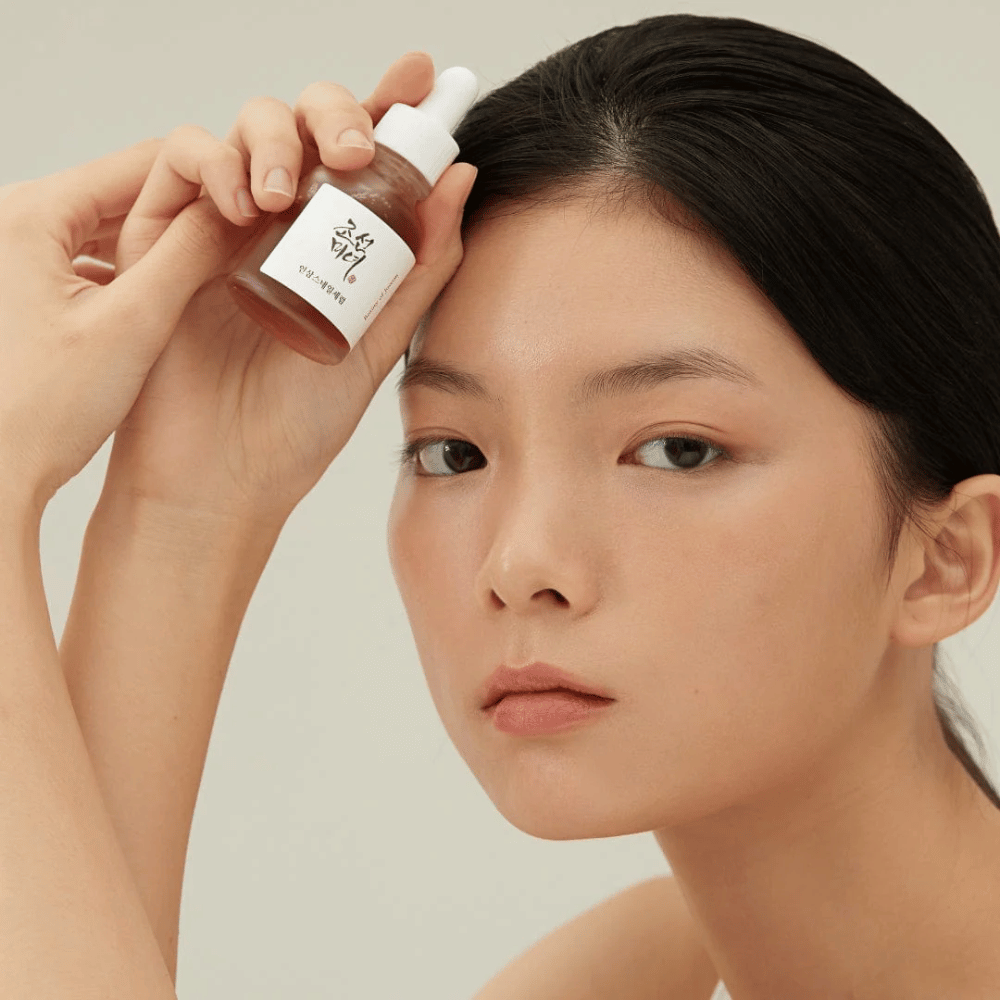 La modelo sostiene Beauty of Joseon Revive Serum en la mejilla – suero nutritivo con ginseng y snail mucin.