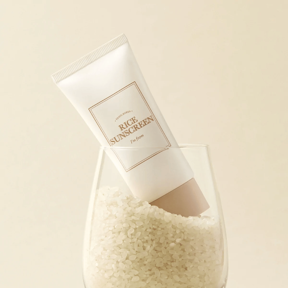 Tubo con "I'm from" Rice Sunscreen, SPF50+ PA++++, colocado en un vaso con granos de arroz.