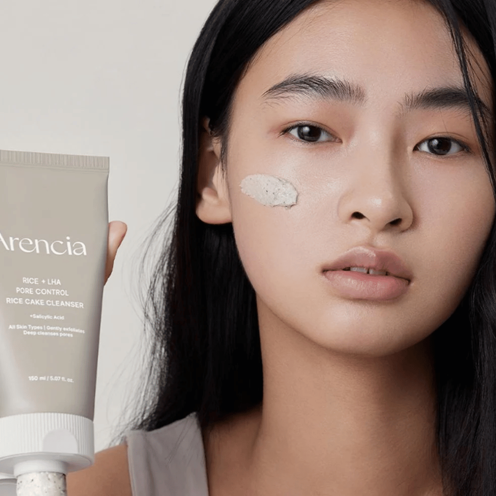 Modelo sosteniendo Arencia Rice + LHA Pore Control Rice Cake Cleanser con producto aplicado en la mejilla, ilustra una limpieza de poros suave pero efectiva para uso diario.