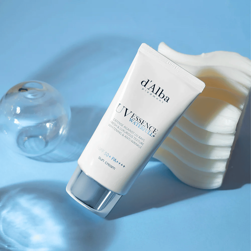 d'Alba UV Essence Waterfull+ Sun Cream con SPF 50+ PA++++ se encuentra sobre un fondo azul con reflejos de luz y elementos decorativos, destacando las propiedades frescas e hidratantes de la crema solar.