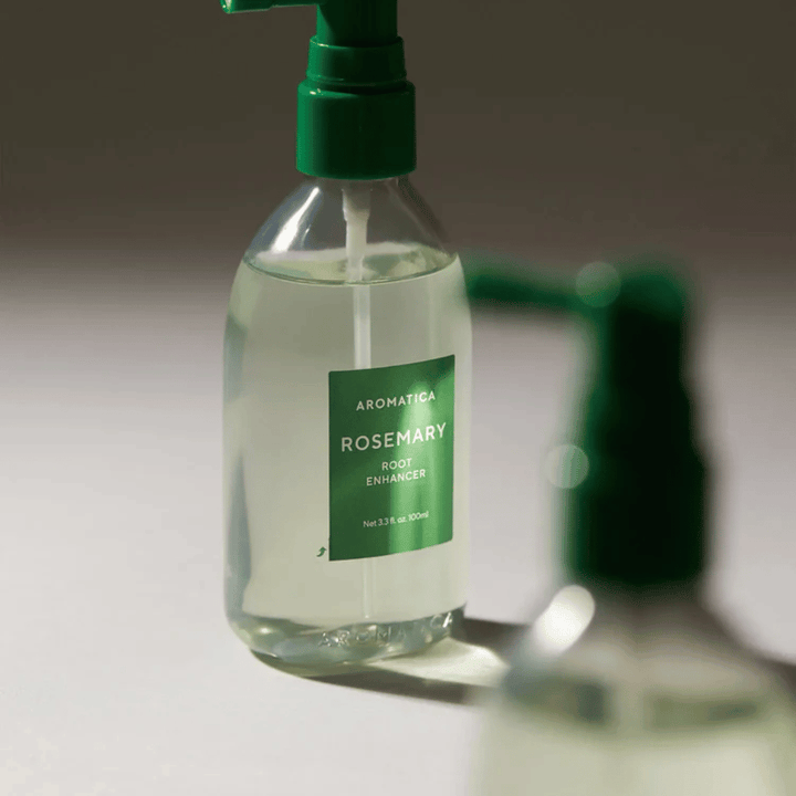 Primer plano de AROMATICA Rosemary Root Enhancer con boquilla aplicadora verde. La imagen se centra en el diseño de la botella y la aplicación precisa directamente sobre el cuero cabelludo.