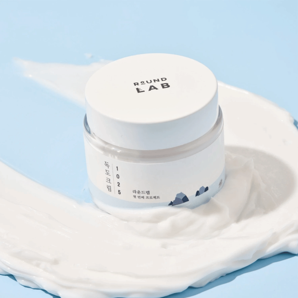 Un frasco con Round Labs 1025 Dokdo Cream 80 ml que proporciona hidratación, colocado sobre un fondo azul vibrante.