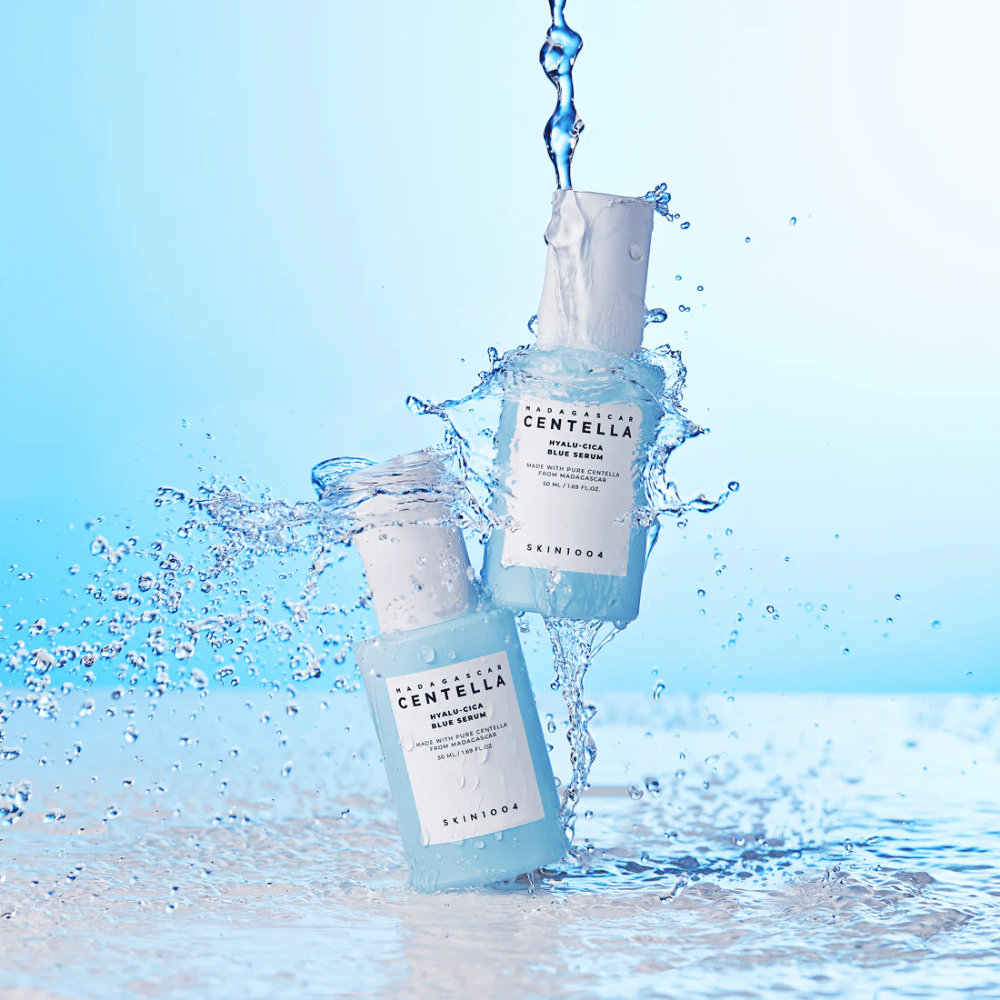 Dos botellas de SKIN1004 Madagascar Centella Hyalu-Cica Blue Serum son alcanzadas por una cascada de agua contra un fondo azul claro.
