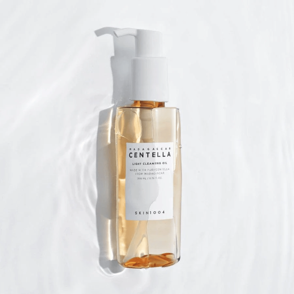 SKIN1004 Madagascar Centella Light Cleansing Oil sobre fondo blanco con suaves reflejos de agua que destacan la botella transparente y el contenido dorado.