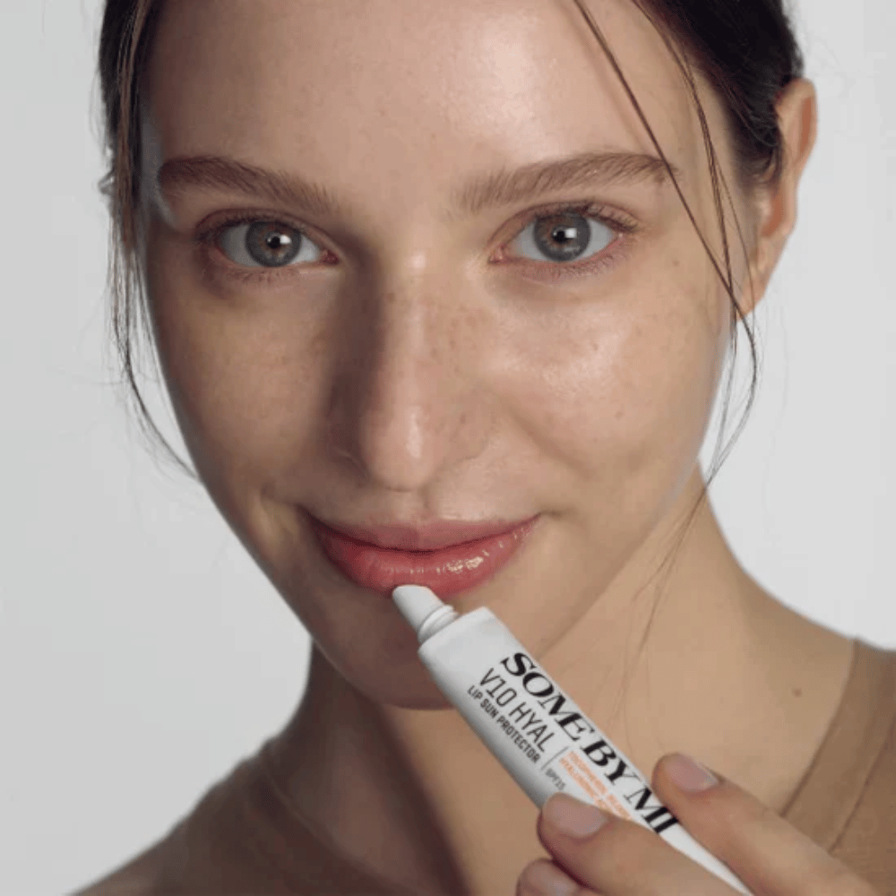 Una mujer sostiene un tubo V10 Hyal Lip Sun Protector SPF15 bálsamo labial de 7 ml para protección solar e hidratación, de SOME BY MI.