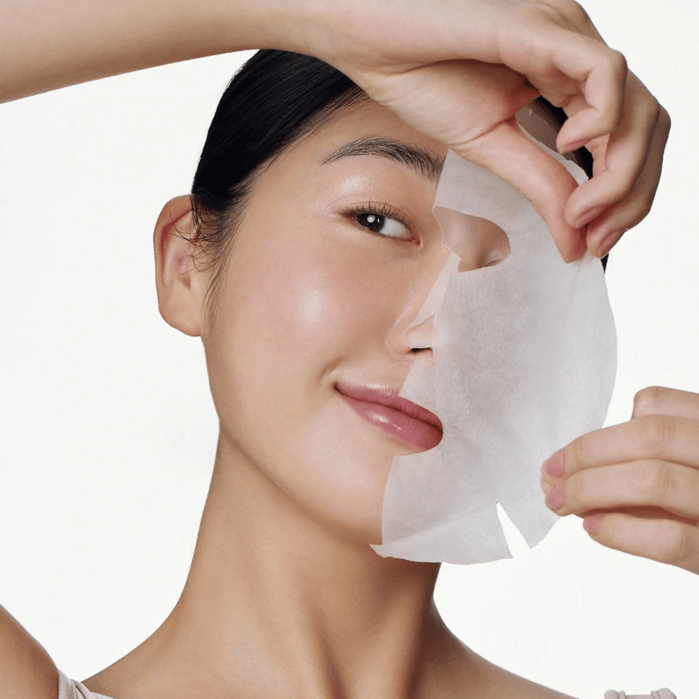 Esta imagen muestra a una persona usando una mascarilla facial, específicamente "Galactomyces Glutathione Daily Mask" de Some By Mi. La mascarilla ilumina la piel y le da un brillo radiante mientras cuida e hidrata profundamente la piel, gracias a ingredientes como el glutatión y la vitamina C.