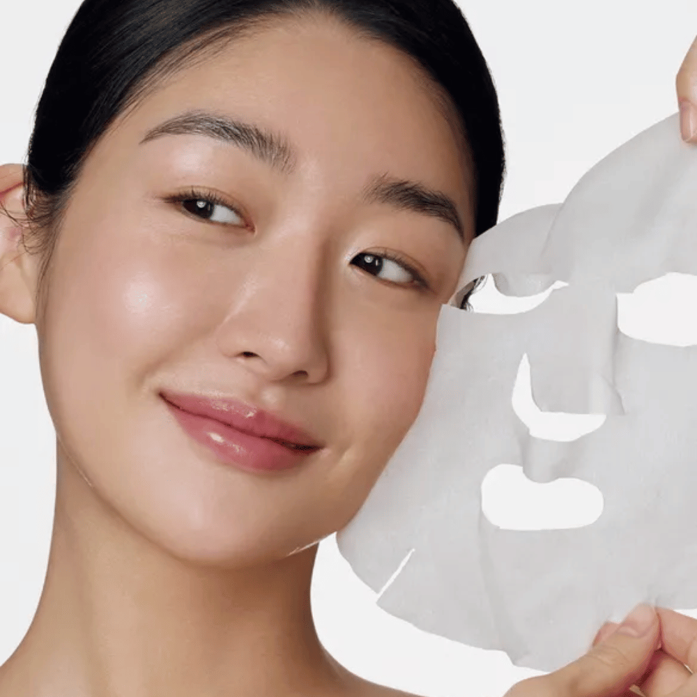 La imagen muestra a una persona usando una mascarilla facial, específicamente una "Retinol Intense Daily Mask" de Some By Mi. La mascarilla está diseñada para uso diario y contiene retinol para mejorar la textura de la piel, reducir líneas finas y dar un tono de piel más uniforme.