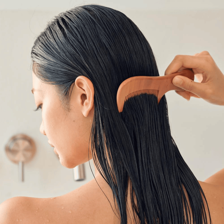 Una persona peina el cabello largo y húmedo con un peine de dientes anchos después de aplicar Heveblue Salmon Pullkeratin Centella Hair Treatment. Ilustra el efecto desenredante y suavizante para un resultado más liso.