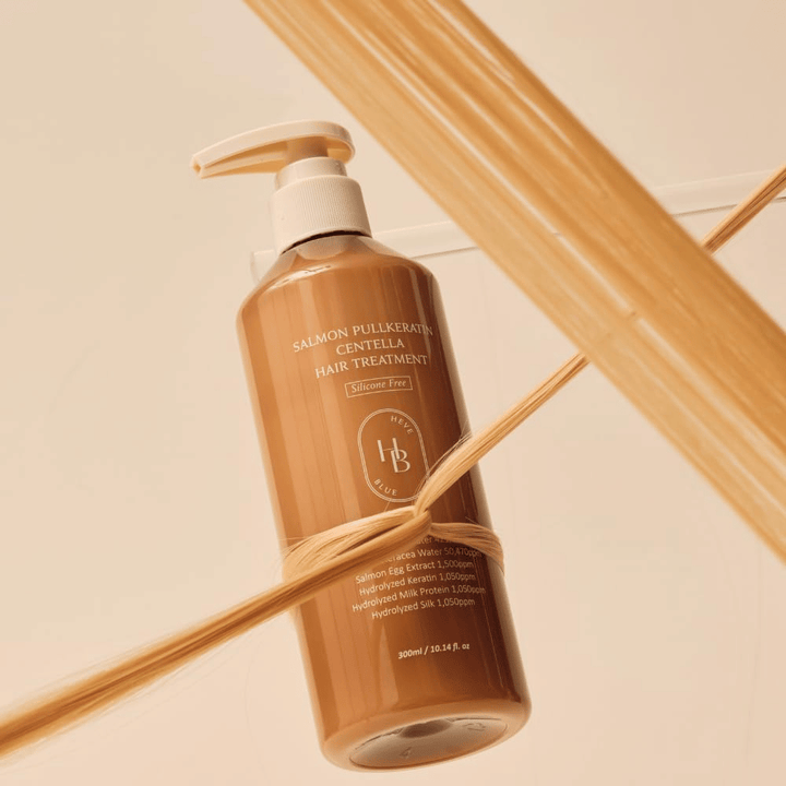 Heveblue Salmon Pullkeratin Centella Hair Treatment en una botella marrón rodeada de mechones de cabello. La imagen destaca las propiedades nutritivas del tratamiento capilar, con enfoque en el brillo, la fuerza y un cabello sedoso.