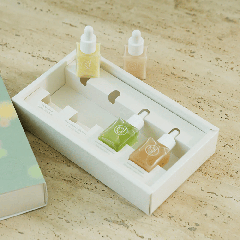 Cuatro frascos de suero coloridos de KAINE Serum Discovery Kit con tapa de pipeta, diseñados para satisfacer diferentes necesidades de la piel en un empaque minimalista y elegante.