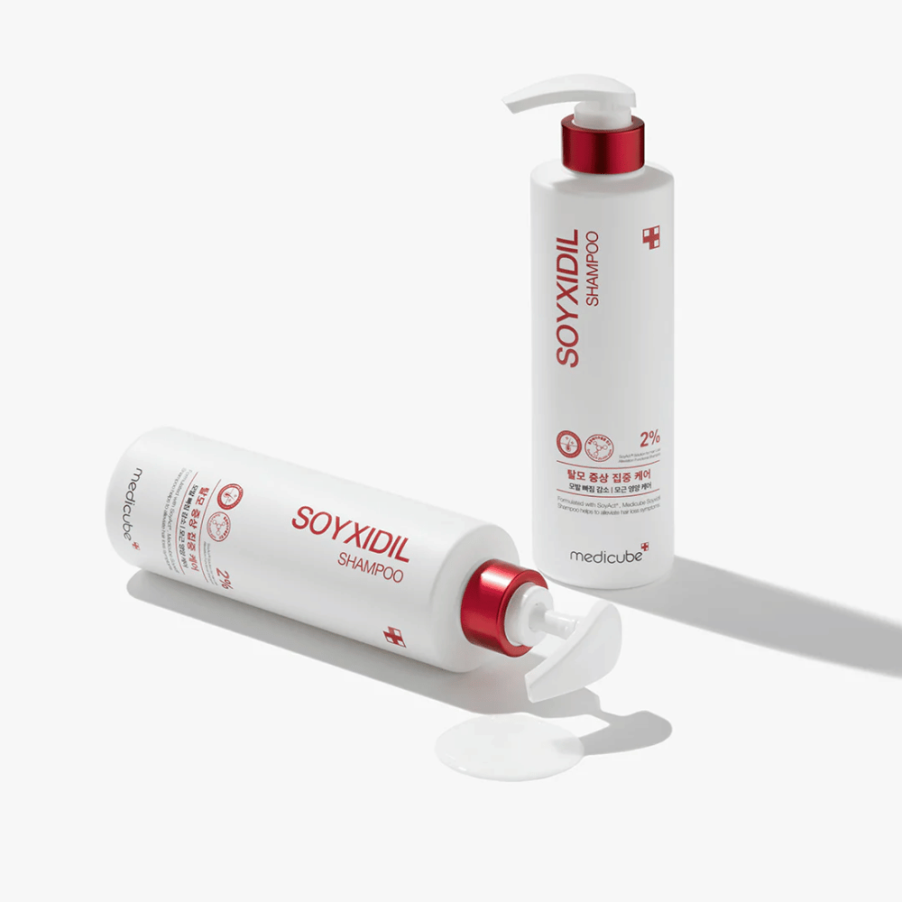 Dos botellas de Medicube Soyxidil Shampoo en diseño blanco y rojo, una de pie y otra acostada con champú derramado al lado.