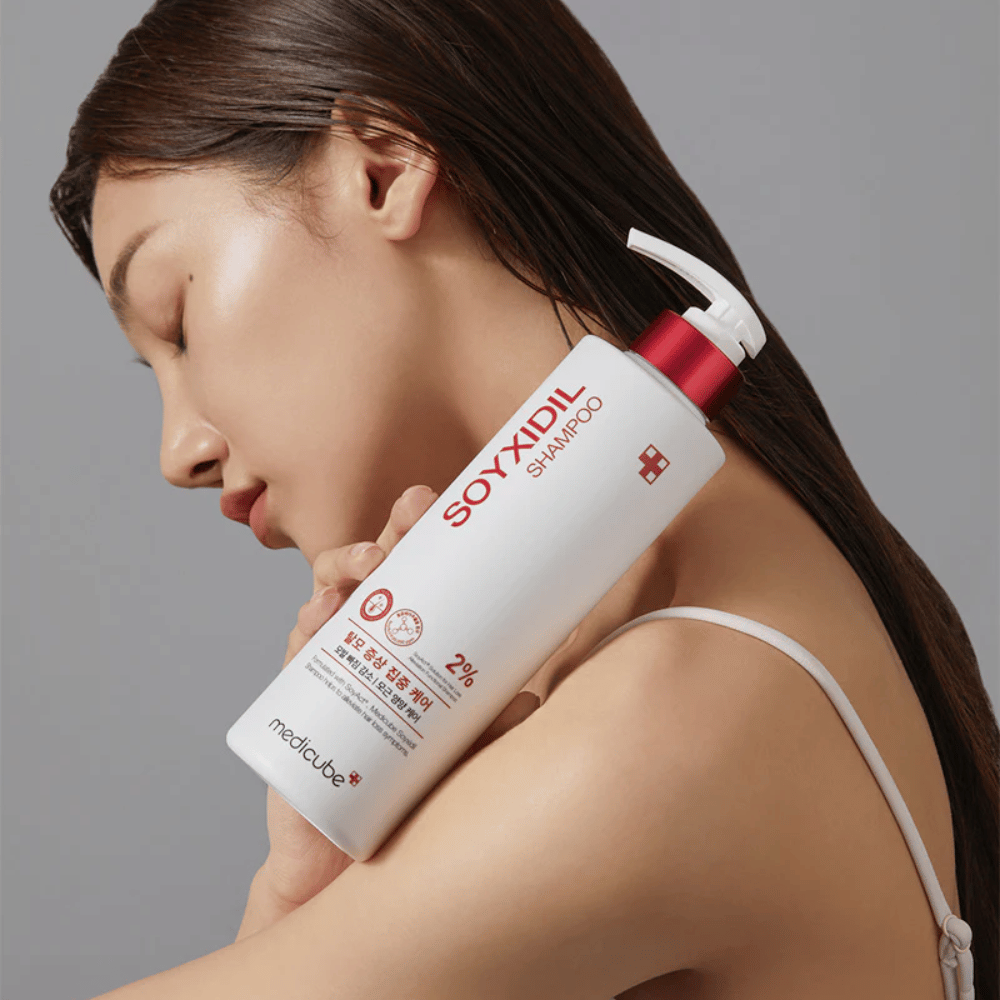 Mujer con cabello largo apoya su cabeza contra una botella de Medicube Soyxidil Shampoo, que fortalece el cuero cabelludo y previene la caída del cabello.